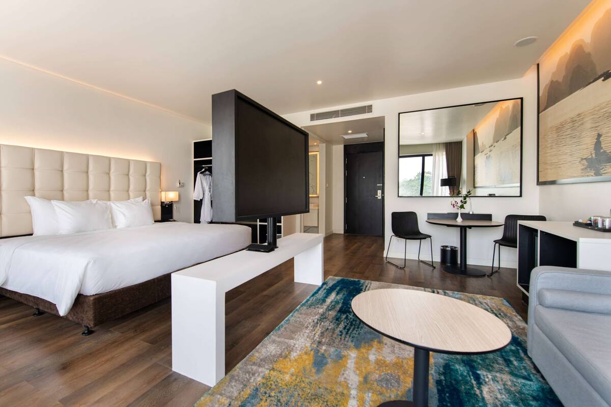 A modern hotel room with a large bed, a desk, a seating area, and a dining table.