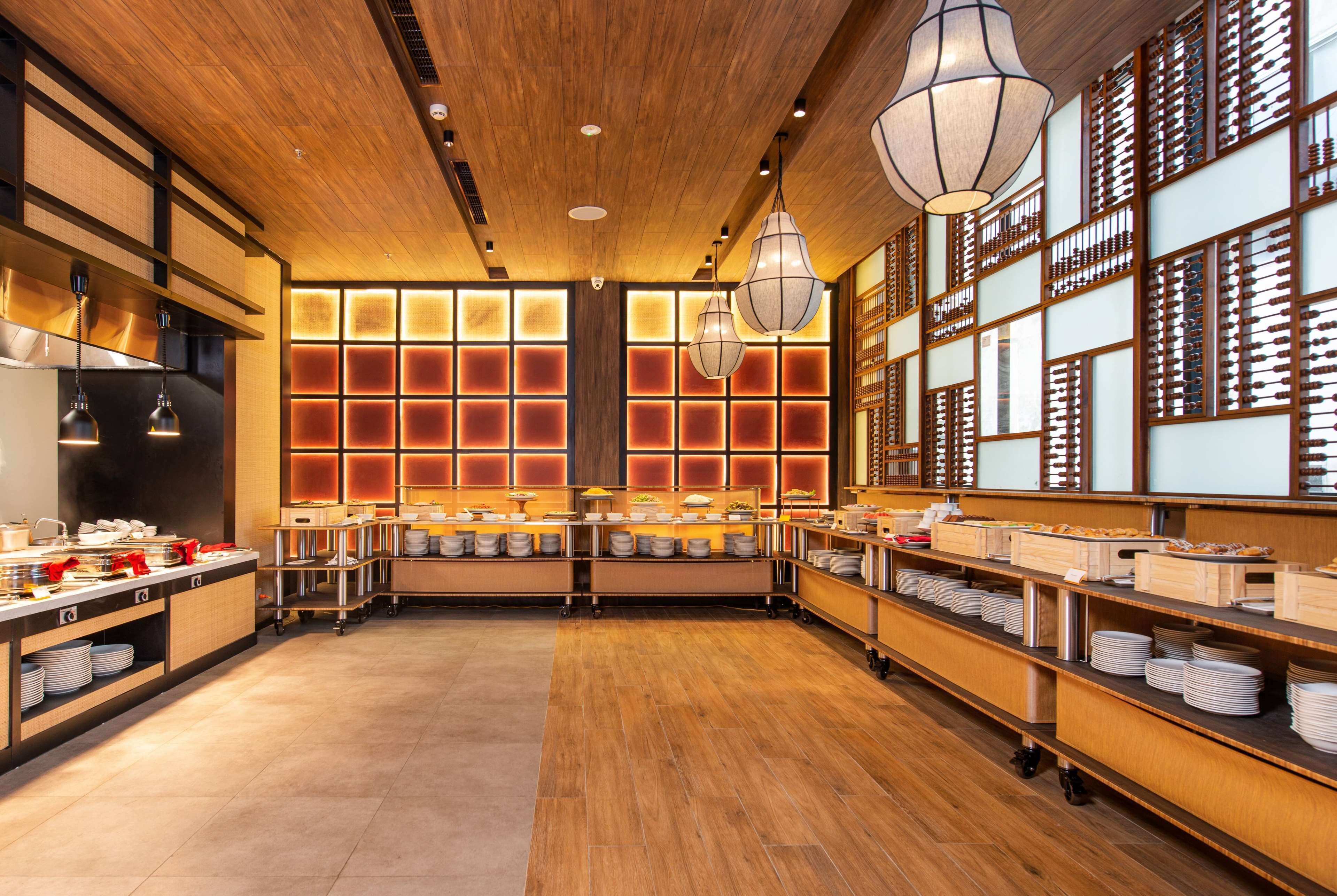A spacious buffet area with wooden flooring, multiple serving stations, and traditional Asian-style lighting.