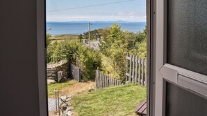Blick aus einem Zimmer mit Fenster auf eine Wiese, eine Steinmauer und einen Holzzaun.
