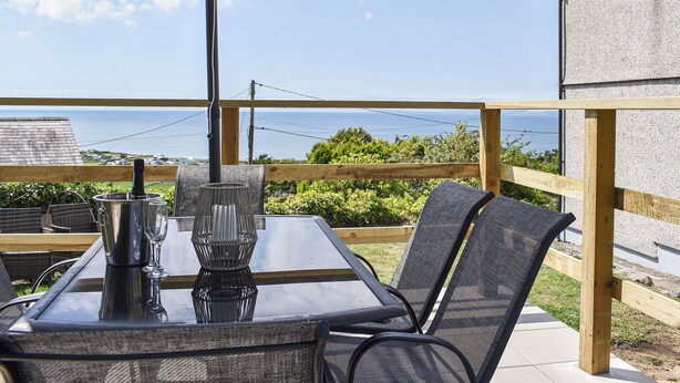 Eine Terrasse im Freien mit Tisch, Stühlen, einem Grill und Blick auf das Meer.