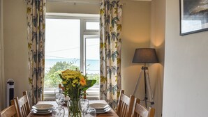 Ein Esszimmer mit Tisch für vier Personen, einem Blumenstrauß und Meerblick durch das Fenster.