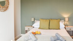 Ein ordentlich bezogenes Bett mit Kissen, Orangensaft auf einem Tablett und Handtüchern.