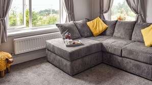 Ein modernes Wohnzimmer mit einer Eckcouch, einer Heizung und einem fenster mit Vorhängen.