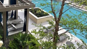 Ein Poolbereich auf dem Dach mit Liegestühlen und einer Pergola, umgeben von einem Gebäude mit Ziegel- und Glasfassade.