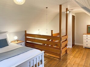 Een slaapkamer met een bed, nachtkastje, houten bedframe, dressoir en een hanglamp.