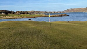 Ein Golfplatz mit Fahne, einem Gewässer und Hügeln in der Ferne.