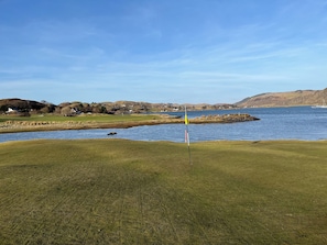 A golf course with a flagstick, water body, and distant hills.