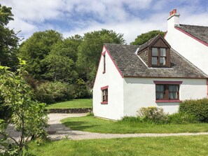 A white house with a red roof and a stone pathway leading to it.
