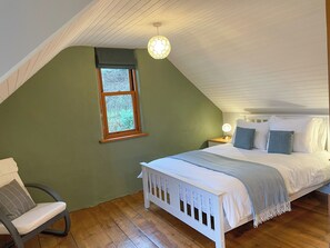A bedroom with a sloped ceiling, a window, a bed with pillows, a chair, and a bedside table with a lamp. - Innish Beag - UK38782 (Clachan Seil)