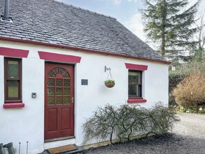 A white building with a red door and windows, a hanging flower basket, and a gravel driveway. - Innish Beag - UK38782 (Clachan Seil)