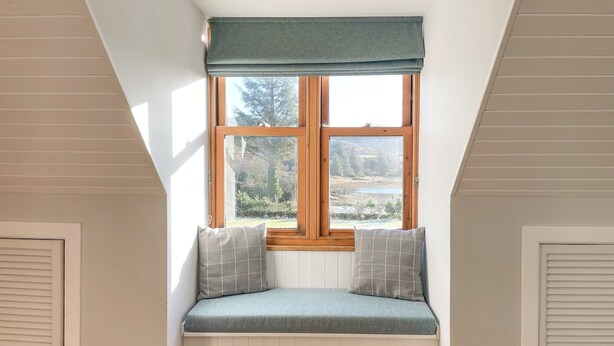 Ein Zimmer mit Fensterbank, weißen Wandverkleidungen und Blick auf einen See und Bäume.