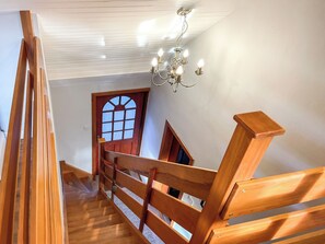 Un escalier en bois avec une rampe, un lustre et une porte dotée d’une fenêtre.