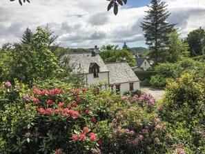 Un bâtiment blanc doté d’un toit en pente, entouré d’une végétation luxuriante et de fleurs roses.