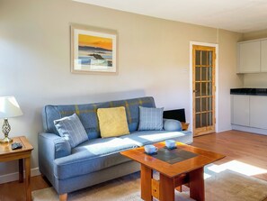 A living room with a sofa, a coffee table, a painting, and a kitchen area.