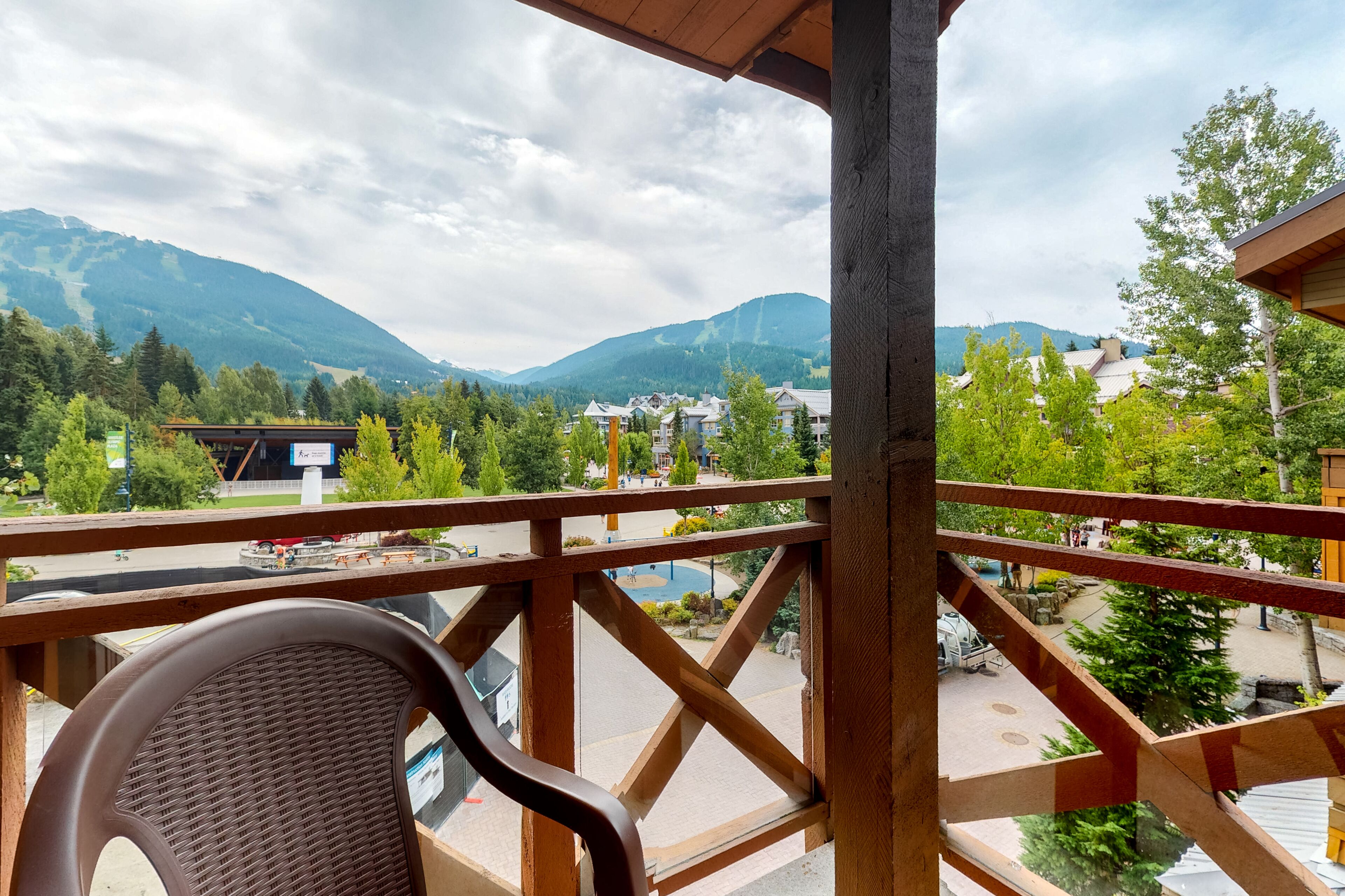 A balcony with a view of mountains, a chair, and a wooden railing.