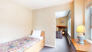 Un dormitorio con cama, tocador, lámpara y vista a una sala de estar con chimenea.