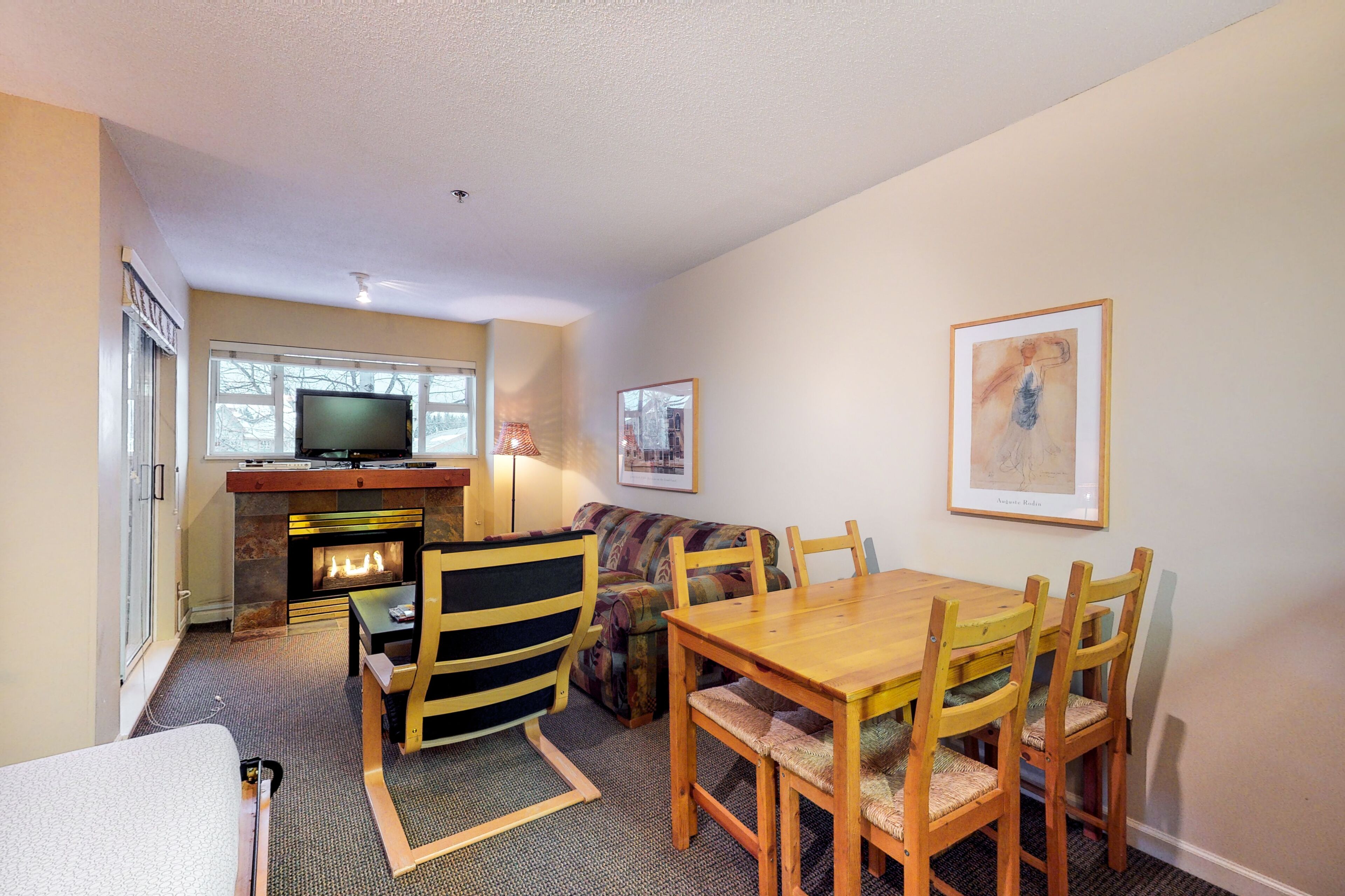 A cozy living room with a fireplace, a television, and a dining area with wooden furniture.