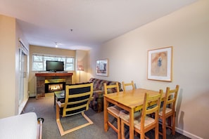 A cozy living room with a fireplace, a television, and a dining area with wooden furniture. - Marketplace Lodge - Whistler Premier (Whistler)