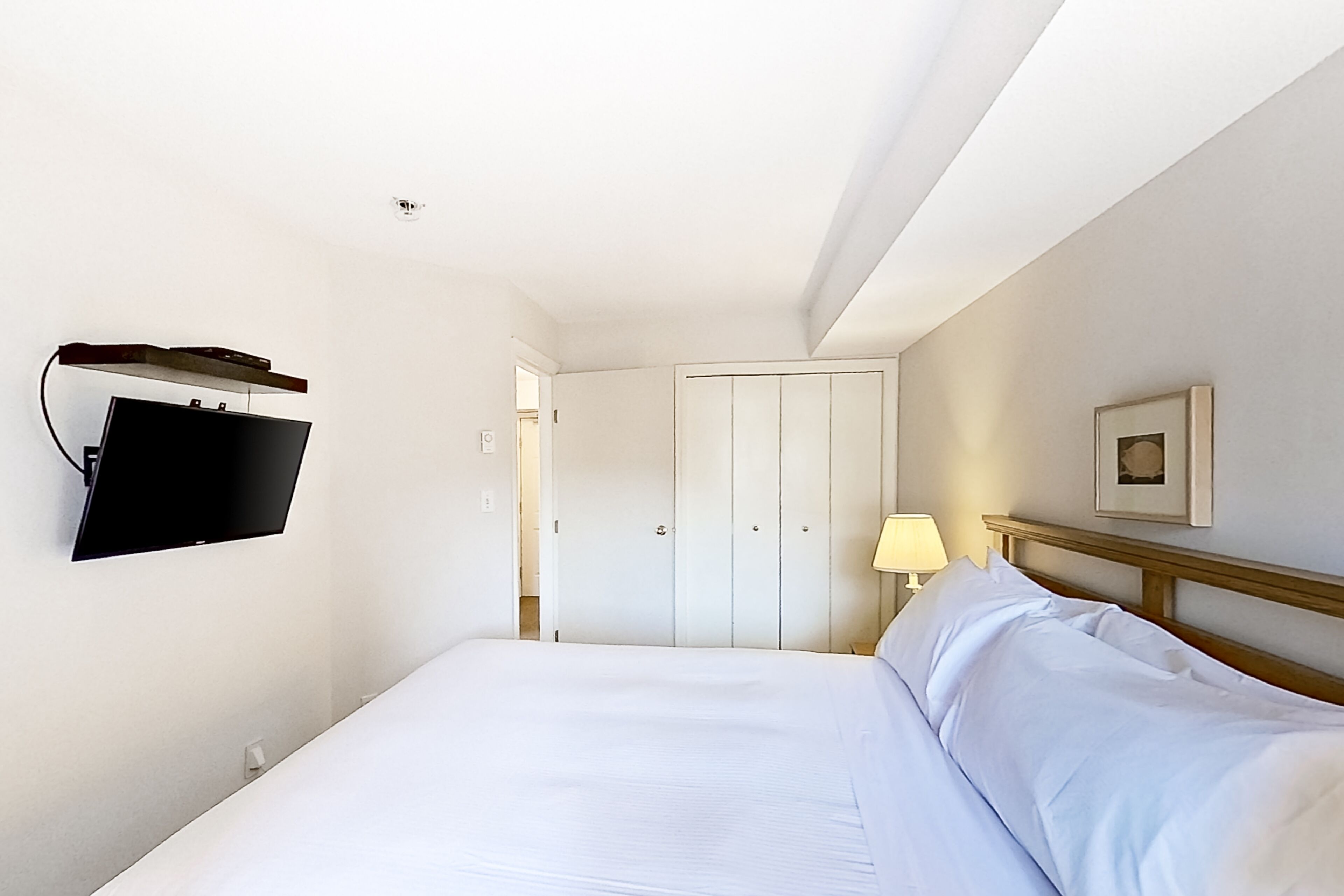 Habitació d'hotel amb un llit, un televisor fixat a la paret, una làmpada de nit i una porta que dona a una altra habitació.