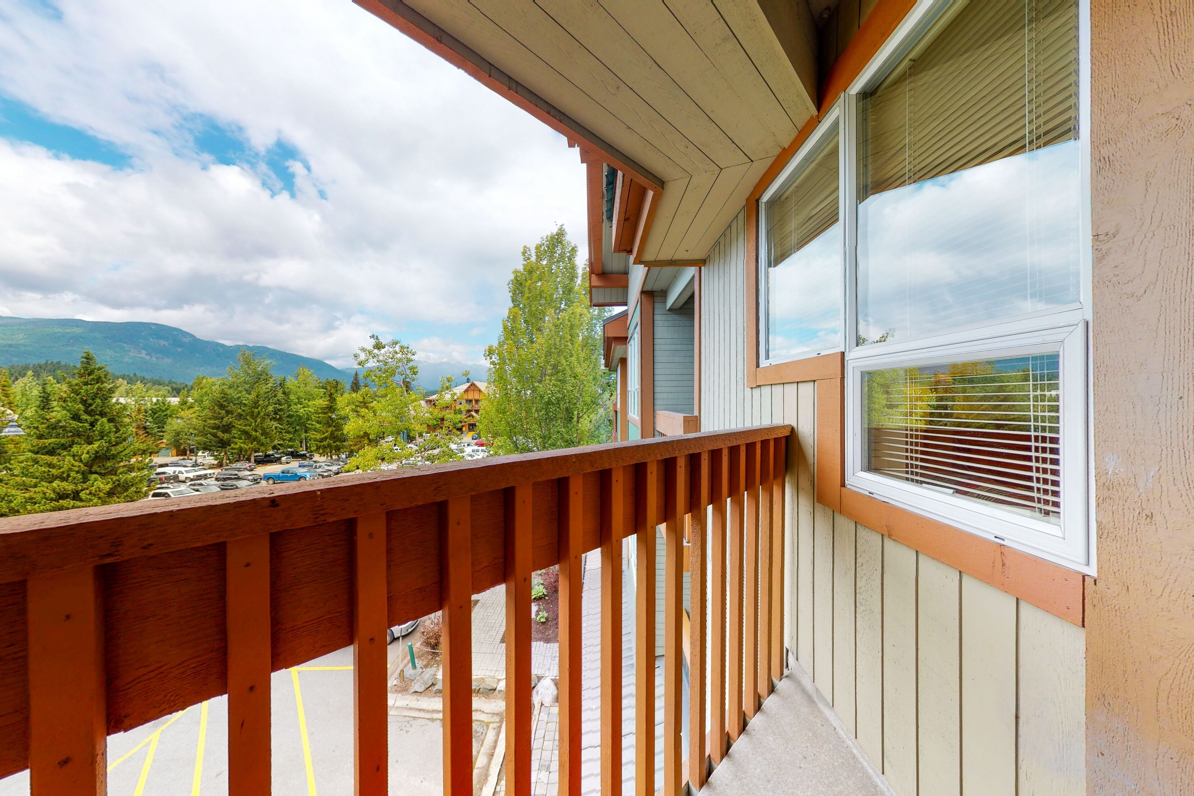 A balcony with a wooden railing overlooking a parking area and a mountainous landscape.