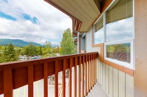 Un balcon doté d’une balustrade en bois, donnant sur un parking et un paysage montagneux.