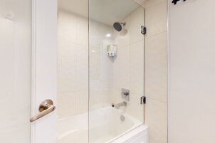 Un baño moderno con ducha de vidrio, bañera blanca y secador de manos.