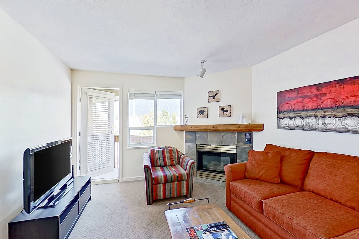 A living room with a TV, a striped armchair, a sofa, a fireplace, and a painting on the wall.