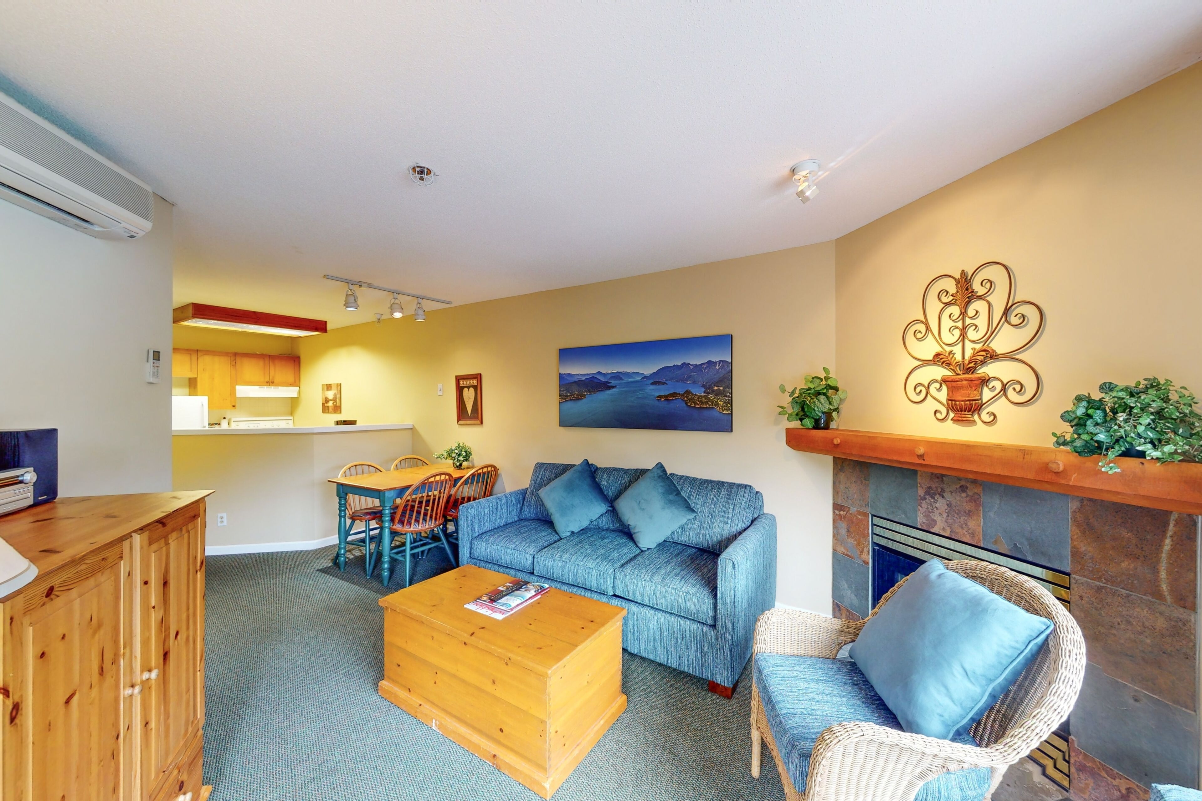 A living room with a blue sofa, a wooden coffee table, a wicker chair, and a fireplace.