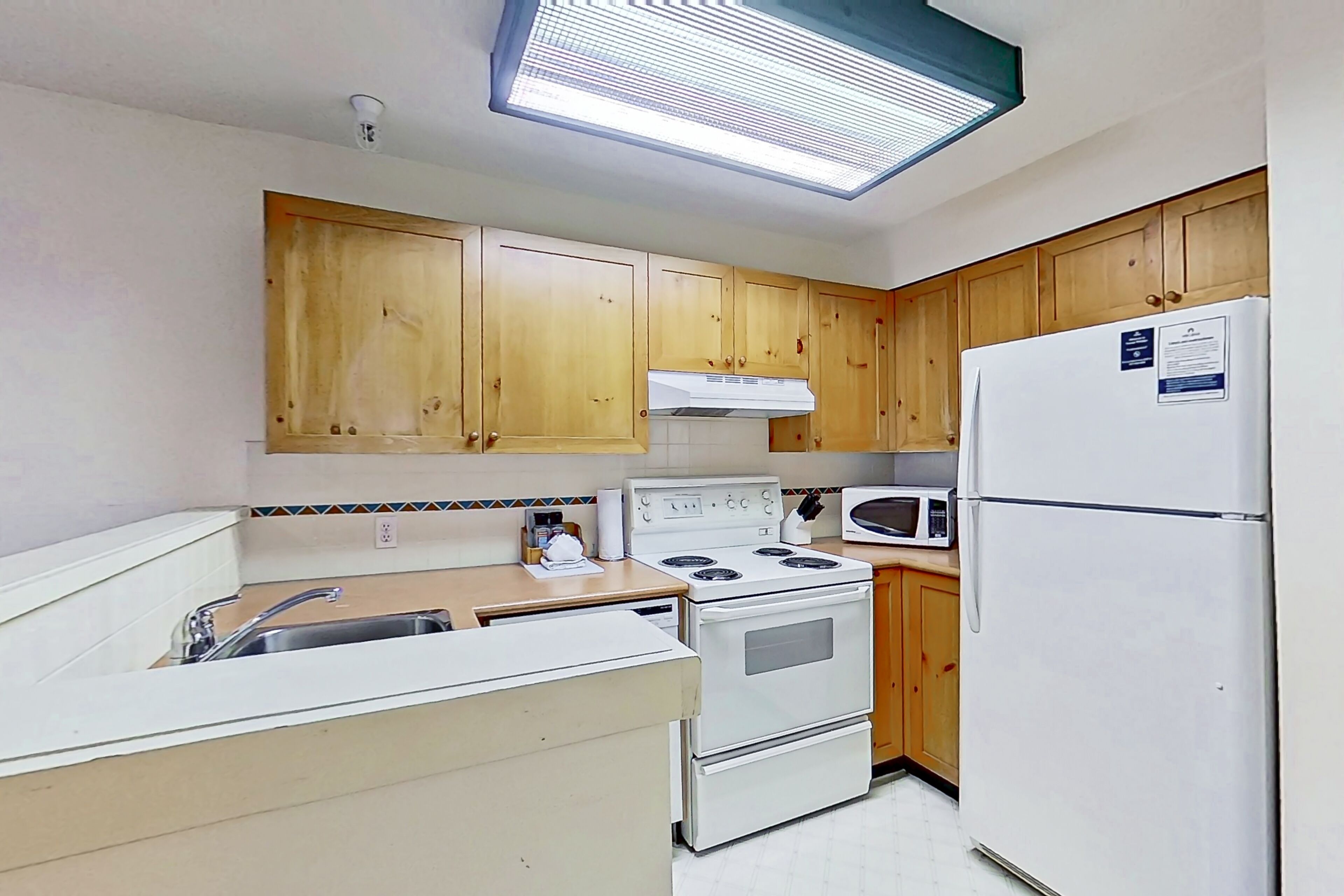 A kitchen with wooden cabinets, a white stove, a microwave, and a refrigerator.