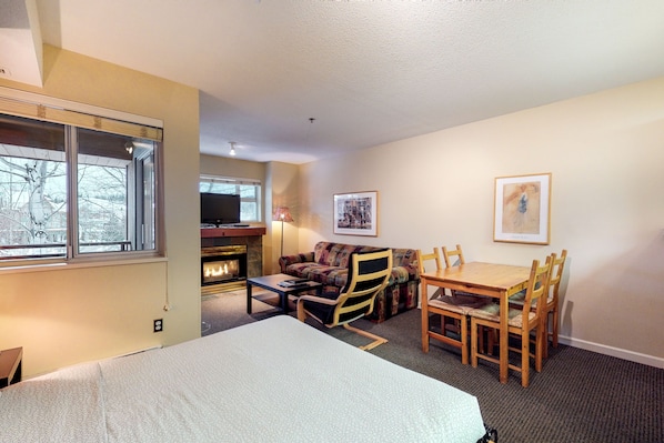A hotel room with a bed, a sofa, a dining table with chairs, a fireplace, and a television. - Marketplace Lodge - Whistler Premier (Whistler)