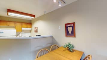A compact kitchen with wooden cabinets, a white countertop, and a dining table with chairs.