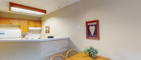 A compact kitchen with wooden cabinets, a white countertop, and a dining table with chairs.
