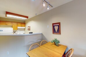 Una cocina compacta con armarios de madera, encimera blanca y una mesa de comedor con sillas.