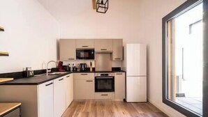 A modern kitchen with light-colored cabinets, a black countertop, and a built-in oven. There is a window on the right side providing natural light. - Apartment Comfortable in the centre of Pau: parking, AC... (Pau)