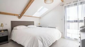 A bedroom with a bed, bedside tables, a hanging light fixture, and a large window with curtains. - Apartment Comfortable in the centre of Pau: parking, AC... (Pau)