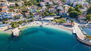 An aerial view of a coastal town with a marina, residential buildings, and a sandy beach.