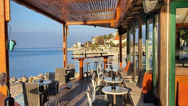 An outdoor seating area with tables and chairs, overlooking a body of water and a coastal town.