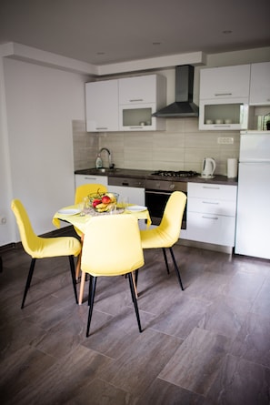 A modern kitchen with white cabinets, a gas stove, and a dining area with yellow chairs and a table set for two.