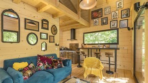 Ein gemütliches Blockhaussinnere mit einem blauen Sofa, einem Holztisch und einer Küchenzeile mit einem großen Fenster.