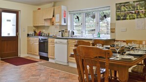 A kitchen with wooden cabinets, a dishwasher, and a dining area with a table set for four. - 3 bedroom accommodation in Llanfair Caereinion, near Welshpool (Llanfair Caereinion, near Welshpool)