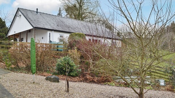 A white house with a grey roof, surrounded by a gravel driveway and a wooden fence. - 3 bedroom accommodation in Llanfair Caereinion, near Welshpool (Llanfair Caereinion, near Welshpool)