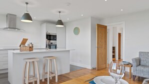 Une cuisine moderne avec un îlot central, des tabourets en bois et une table à manger pour deux personnes, mise avec des assiettes et un verre à vin.
