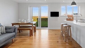 Une cuisine moderne dotée d’une grande fenêtre, d’un plancher en bois et d’un coin repas avec une table dressée pour deux personnes.