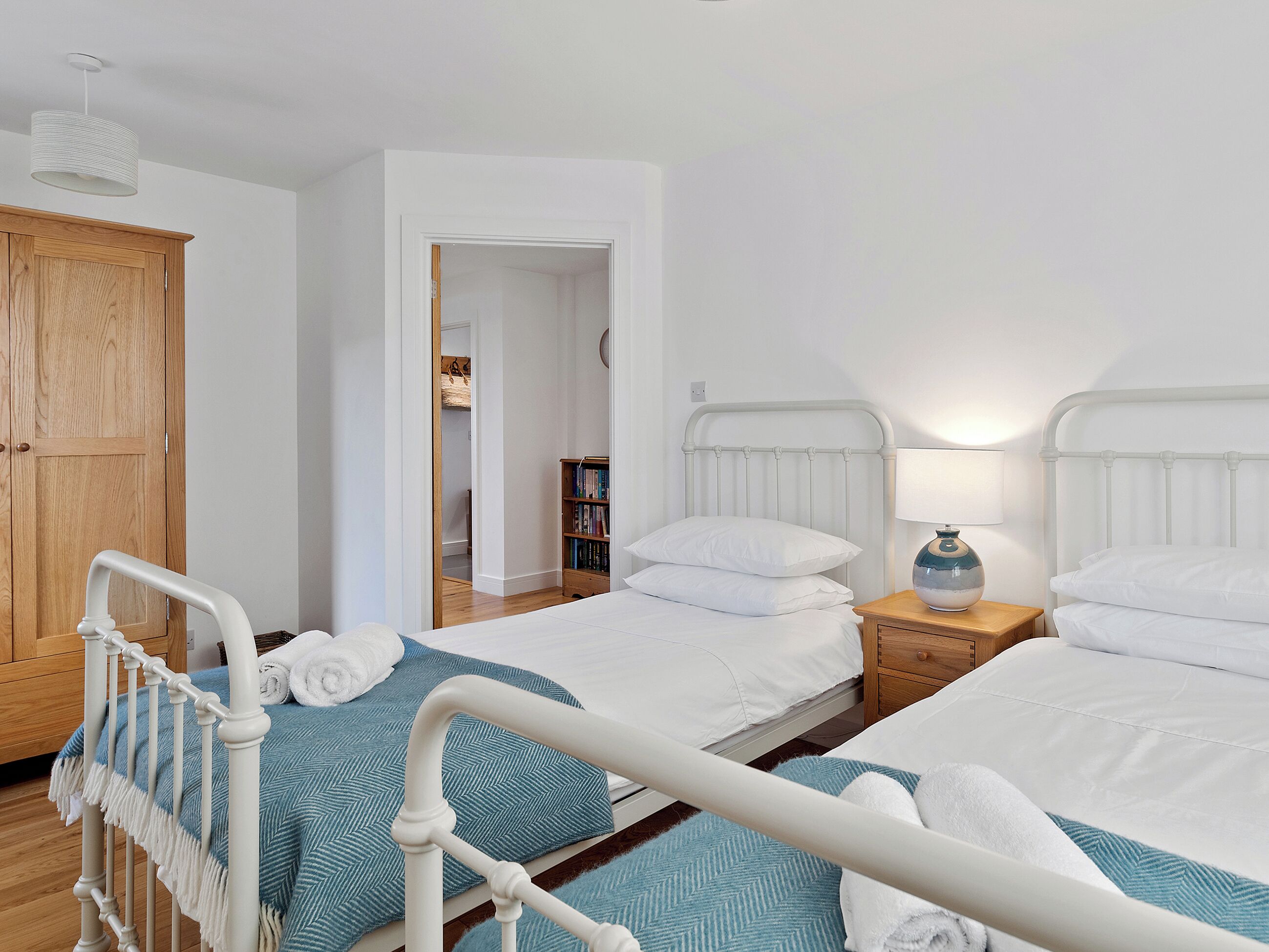 A bedroom with two beds, wooden wardrobe, and a reading area with books.