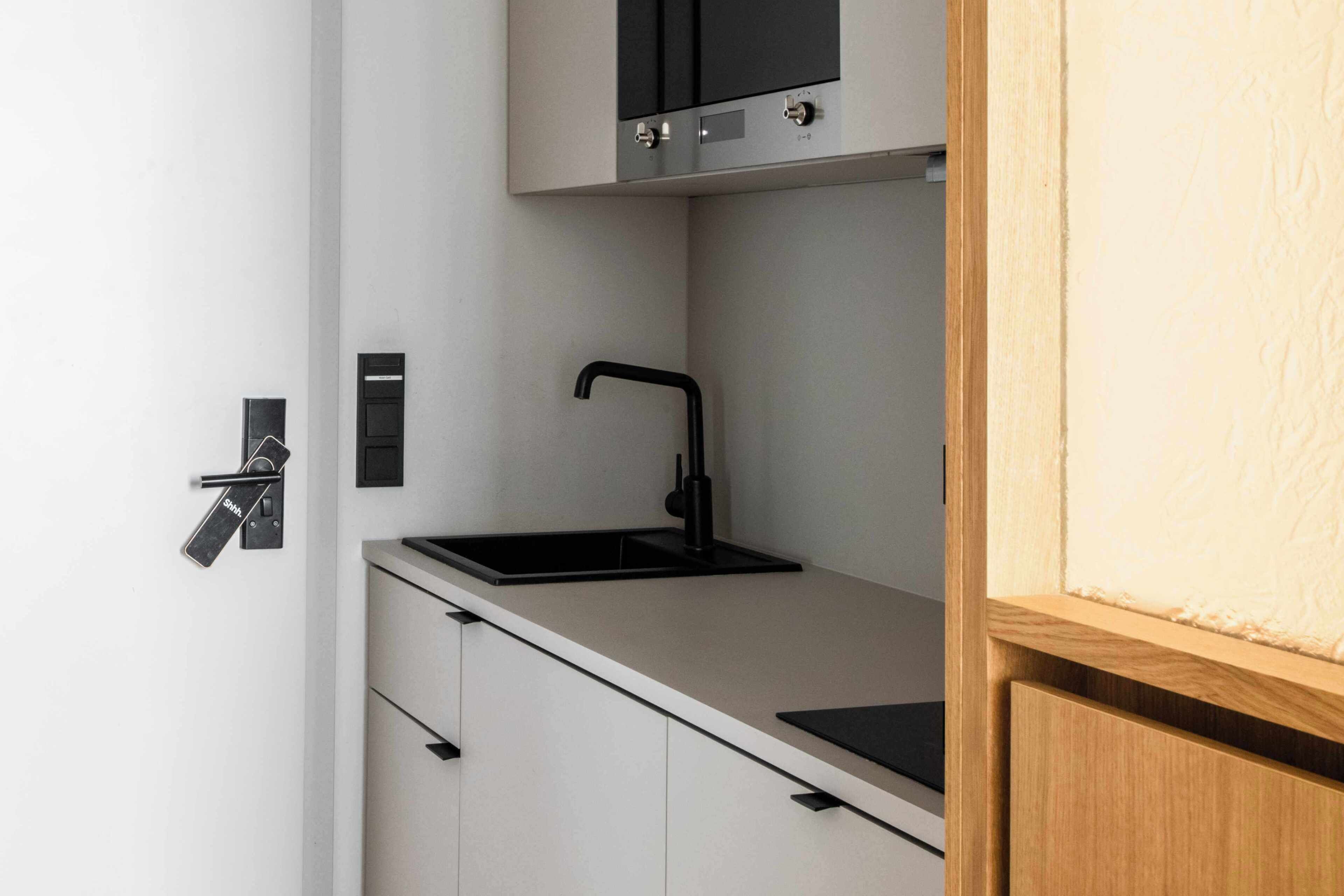 A modern kitchen with a black faucet, a white countertop, and a wooden door.
