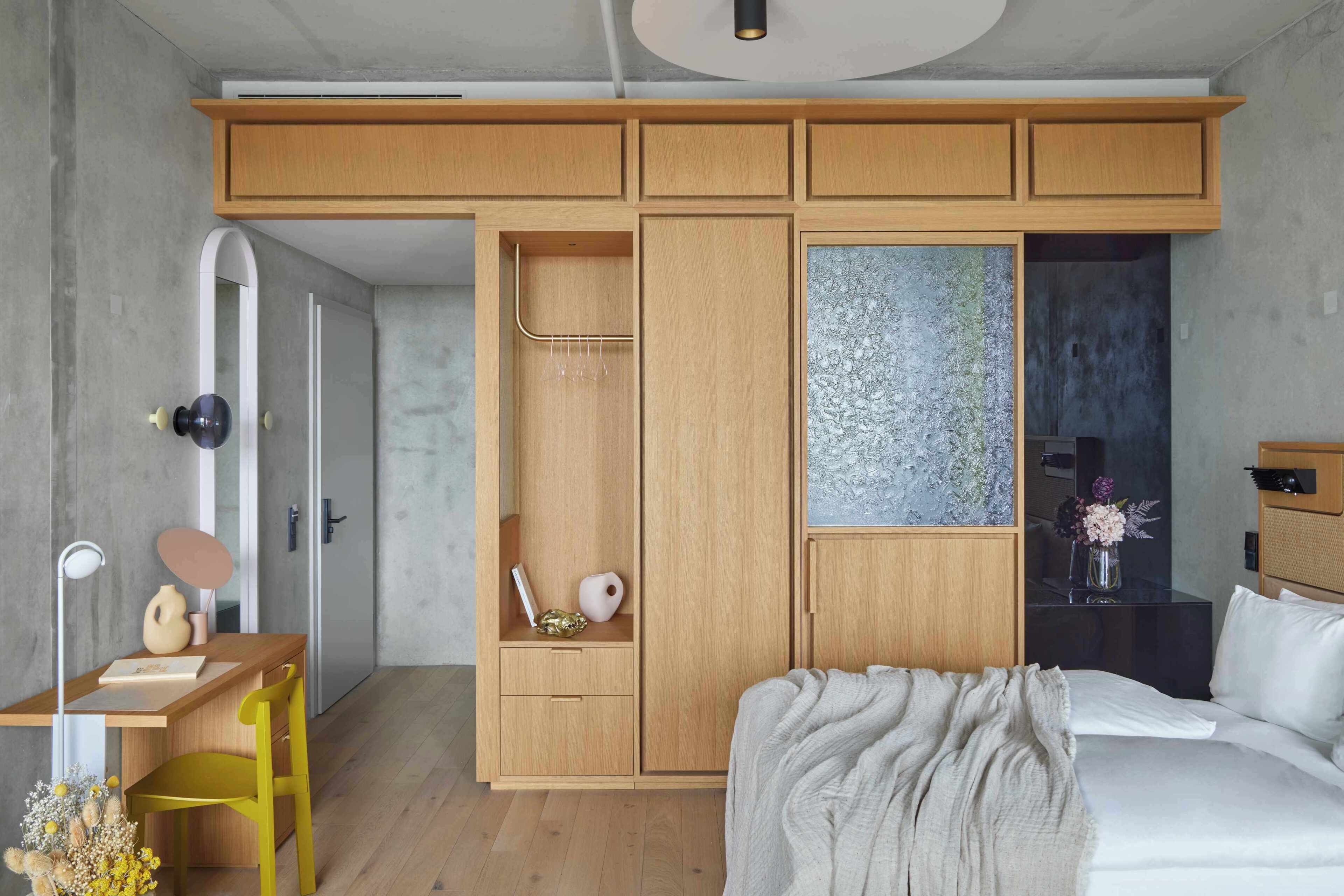 A bedroom with a bed, a desk with a chair, a wardrobe, and a bathroom with a shower.