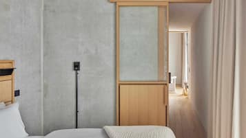 A hotel room with a bed, a wooden headboard, a wall-mounted control panel, and a view of a hallway with a door.