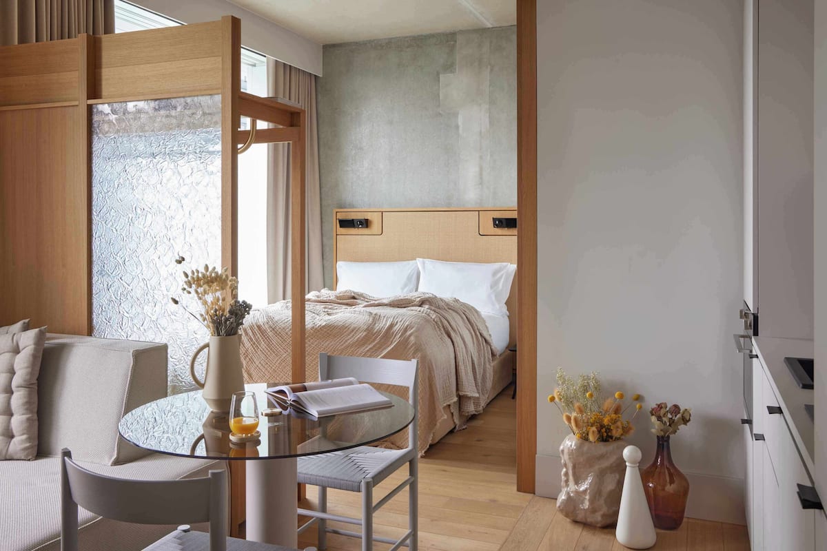 A modern hotel room with a bed, a glass table, a chair, and two vases with flowers.