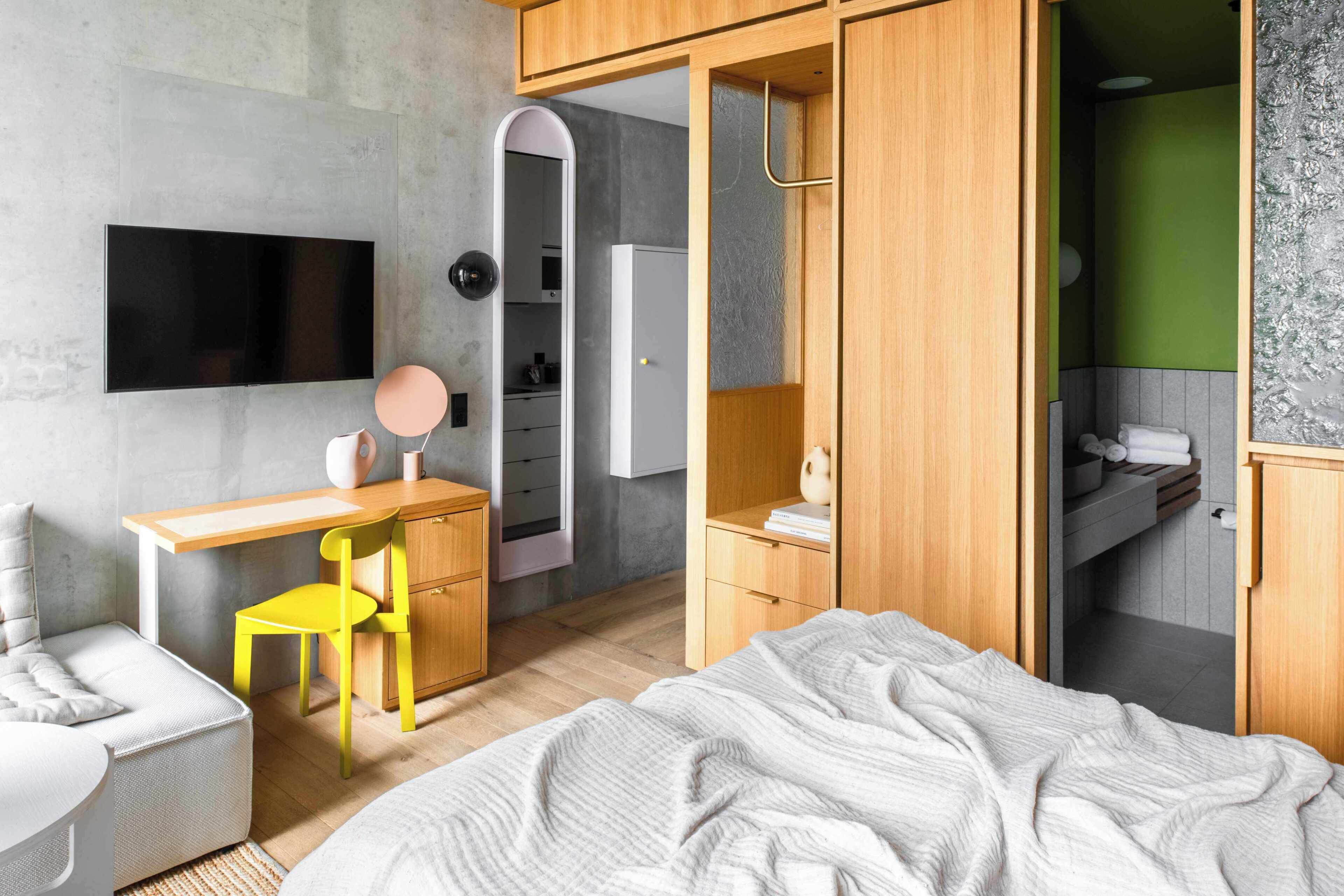 A modern bedroom with a bed, a desk, a chair, a TV, and a wardrobe.