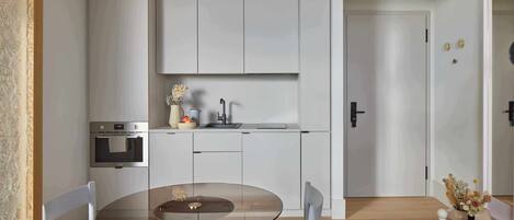 Una cocina moderna con armarios blancos, una mesa de comedor con superficie de vidrio y una pequeña isla con fregadero.